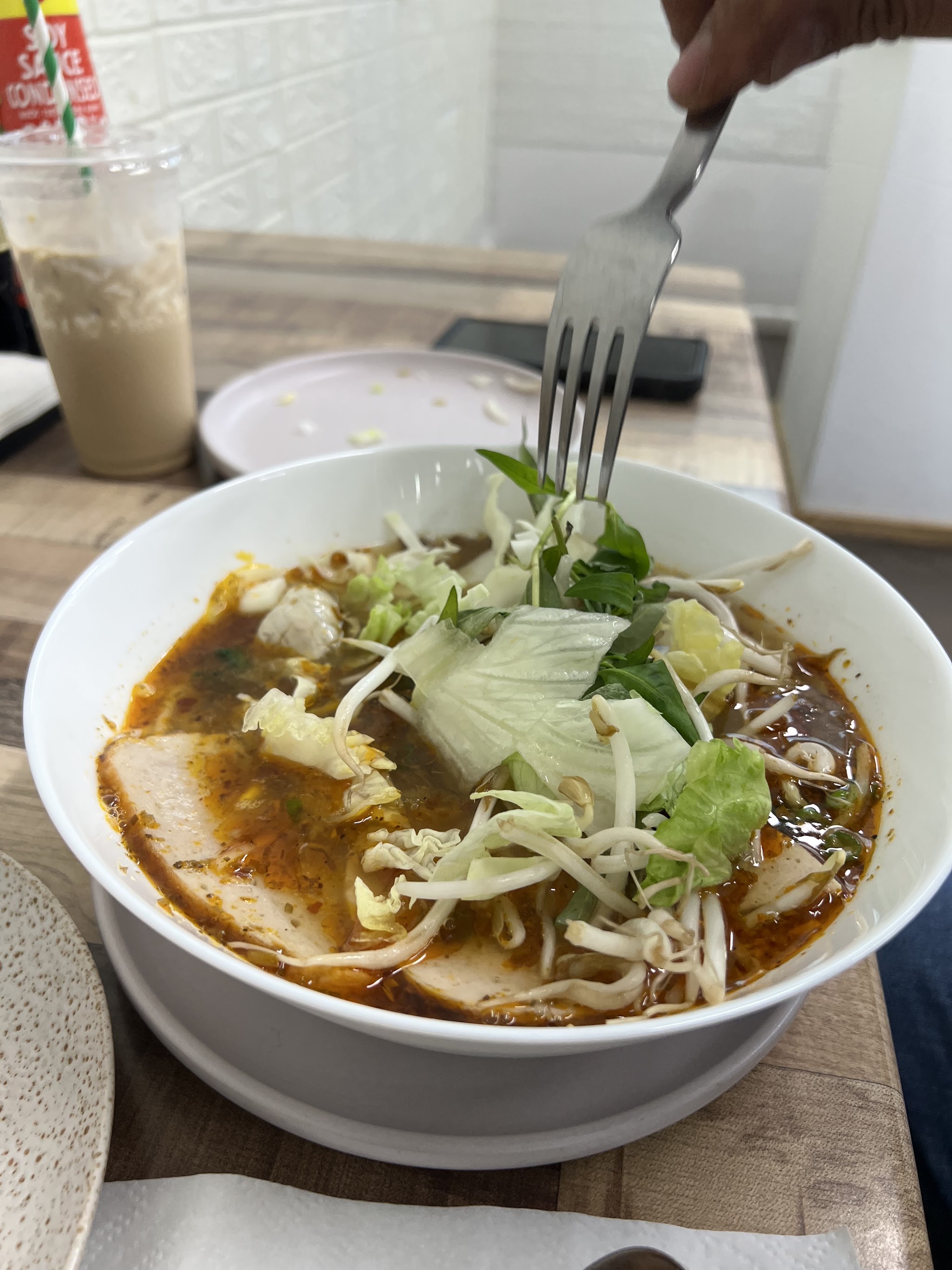 A bowl of spicy noodle soup with pork, bean sprouts and herbs