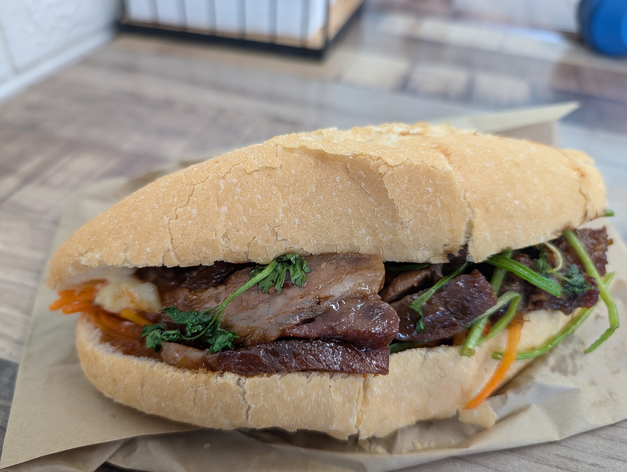 A crackling pork bánh mì cut open, packed with pickled vegetables and herbs