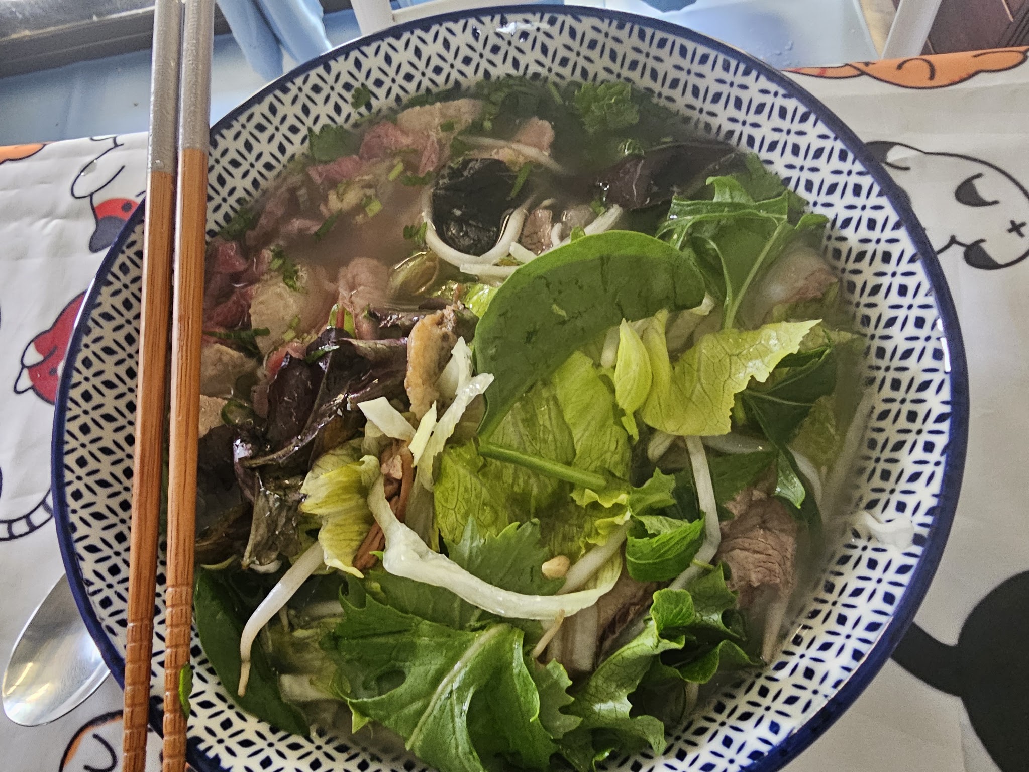 A bowl of Vietnamese noodle soup loaded with fresh greens and herbs